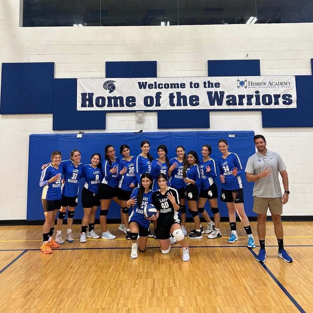 Hebrew Academy girls' volleyball team posing with their trainer in a group photo.