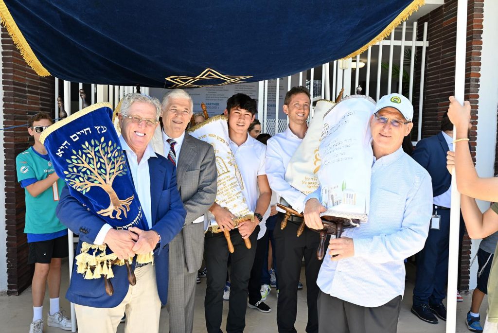 Group of adults happily holding Torah scrolls while taking a photo.