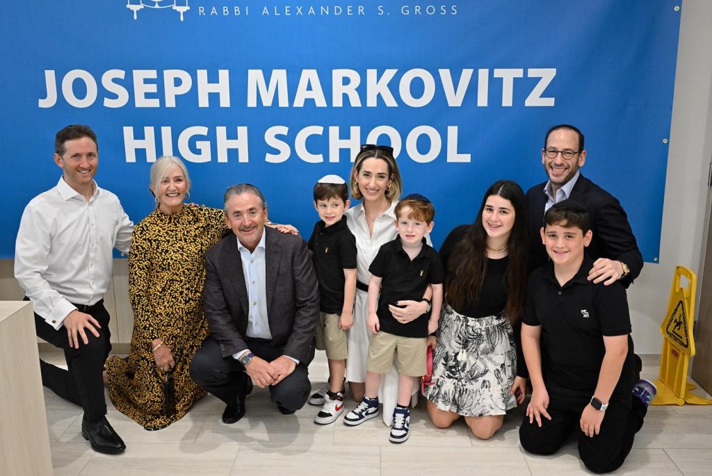 Group photo with kids and adults at Joseph Markovitz High School backdrop banner.