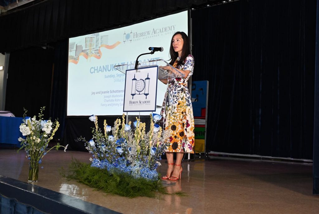 Woman giving a speech at the opening Hebrew Academy celebration with a microphone.