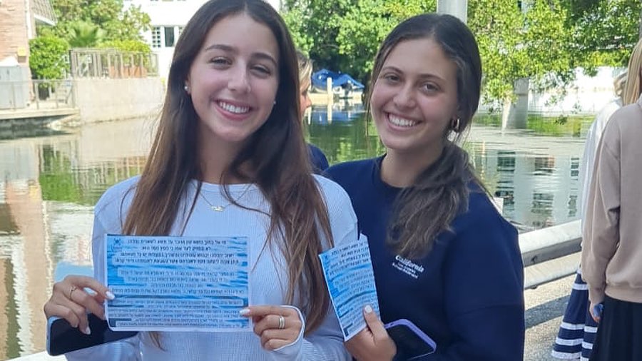 Two students happily showing a list of paper and smiling outdoors.