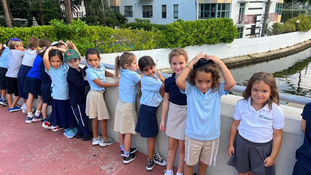 Kids smiling and posing for a photo while holding onto the fence on a bridge outdoors.