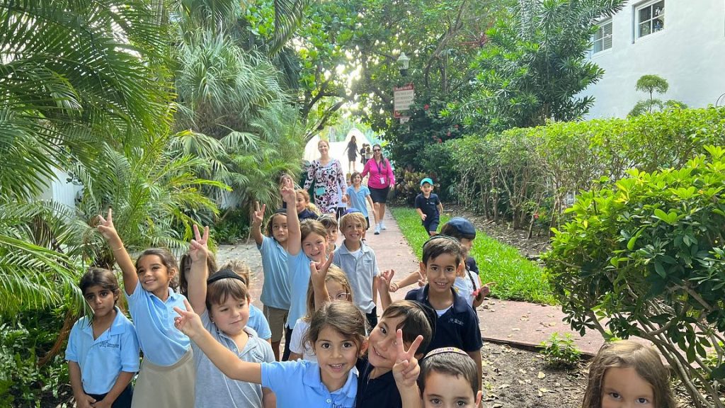 Kids raising their hands with their teacher outdoors while walking.