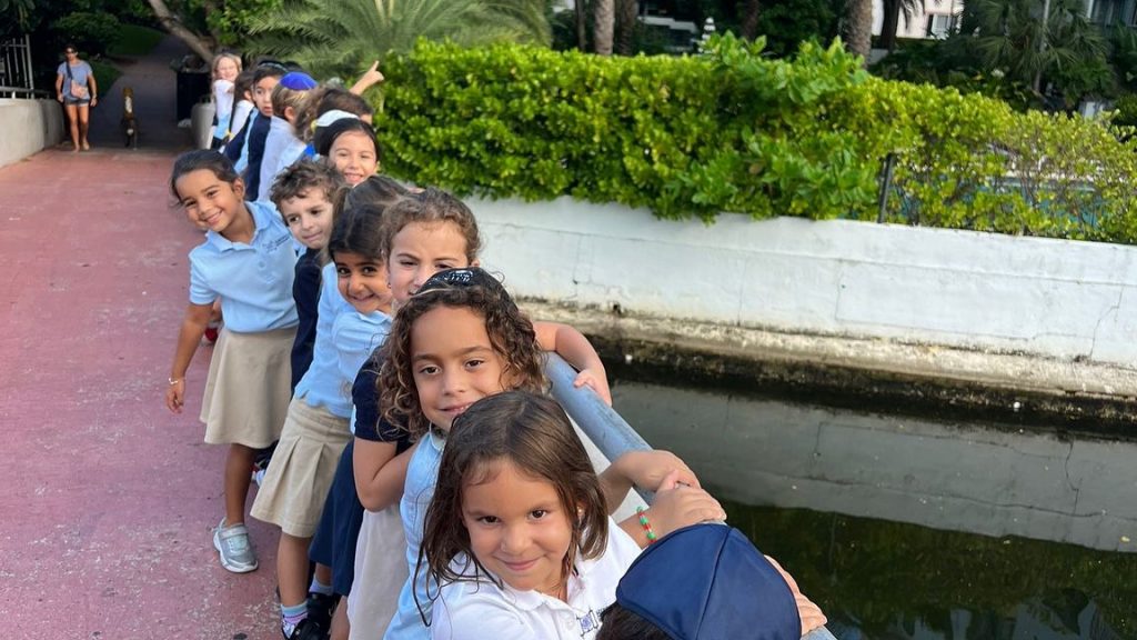 Happy kids holding onto the fence and smiling while standing on a bridge outdoors.