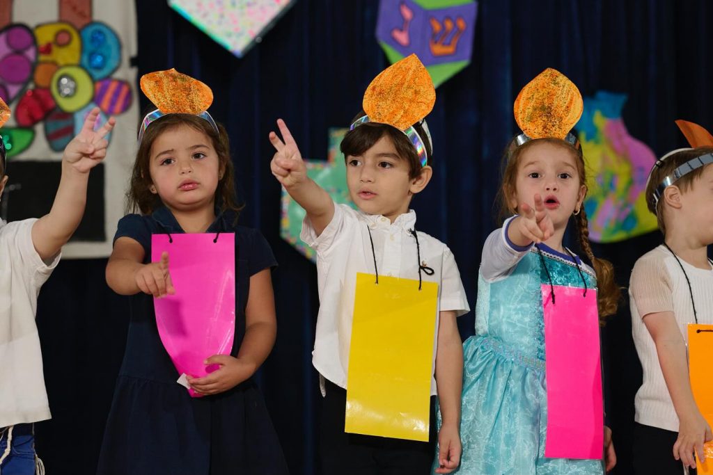 Group of kids with hands raised and showing two fingers, as if answering a question.