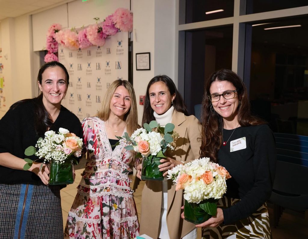 Four parents smiling with flowers at a Hebrew Academy PTSA event.