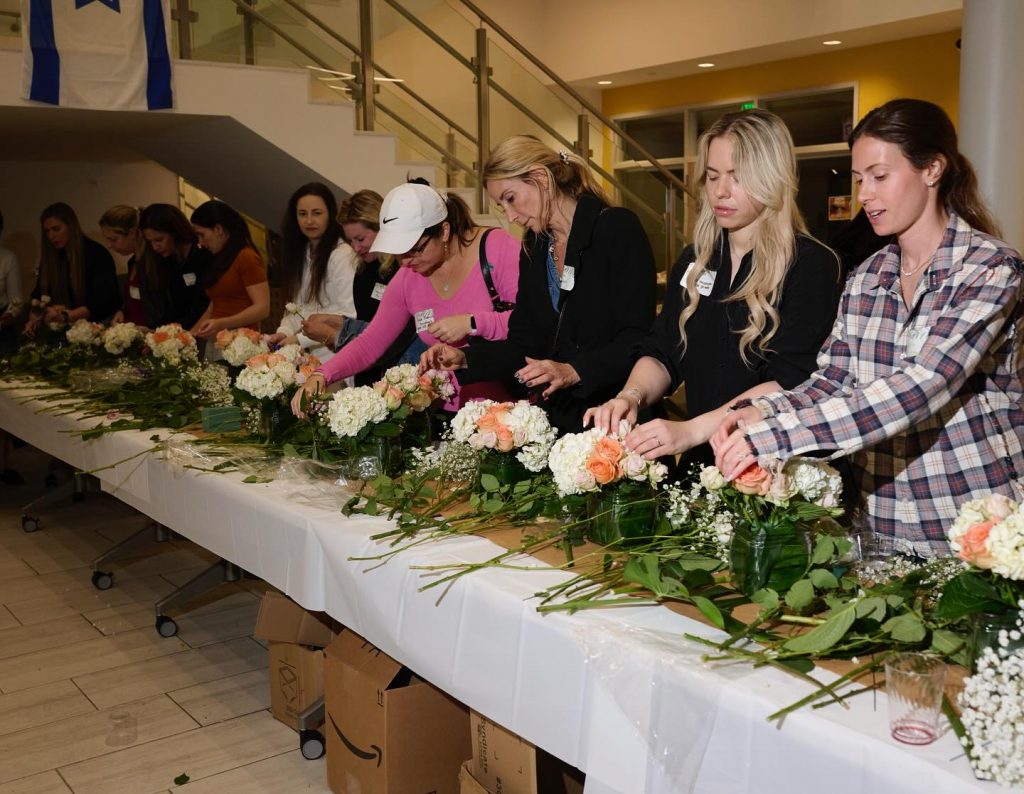 Parents in a flower workshop at an HA PTSA event with an Israeli flag.