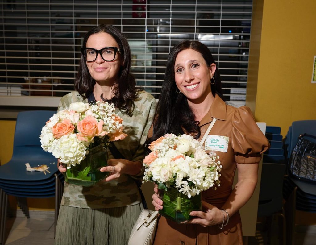 Two women smiling at a Hebrew Academy HA PTSA event with flowers in their hands.