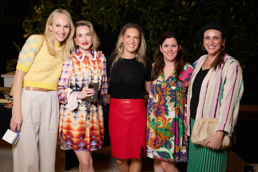 Five adult women smiling for a photo at an outdoor evening event.