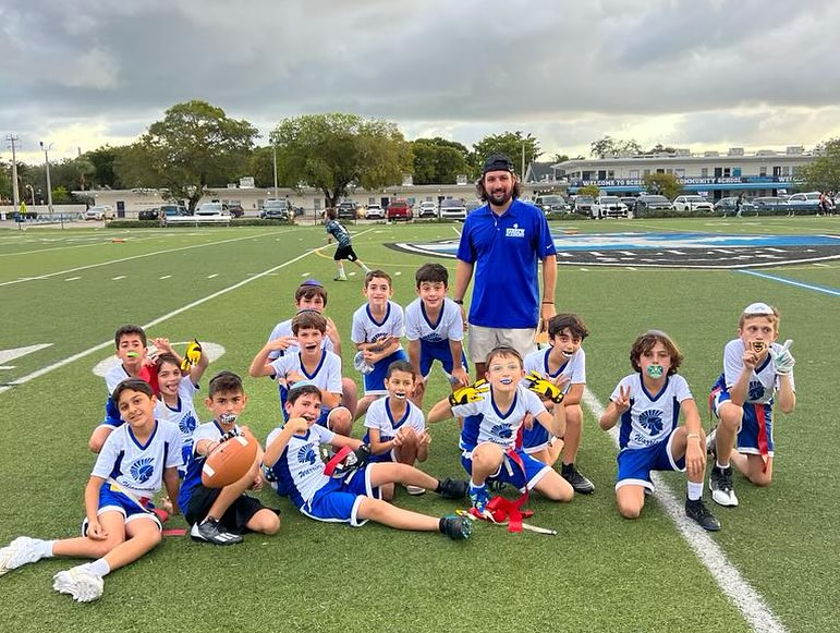 A group of children on a rugby field with their trainer.