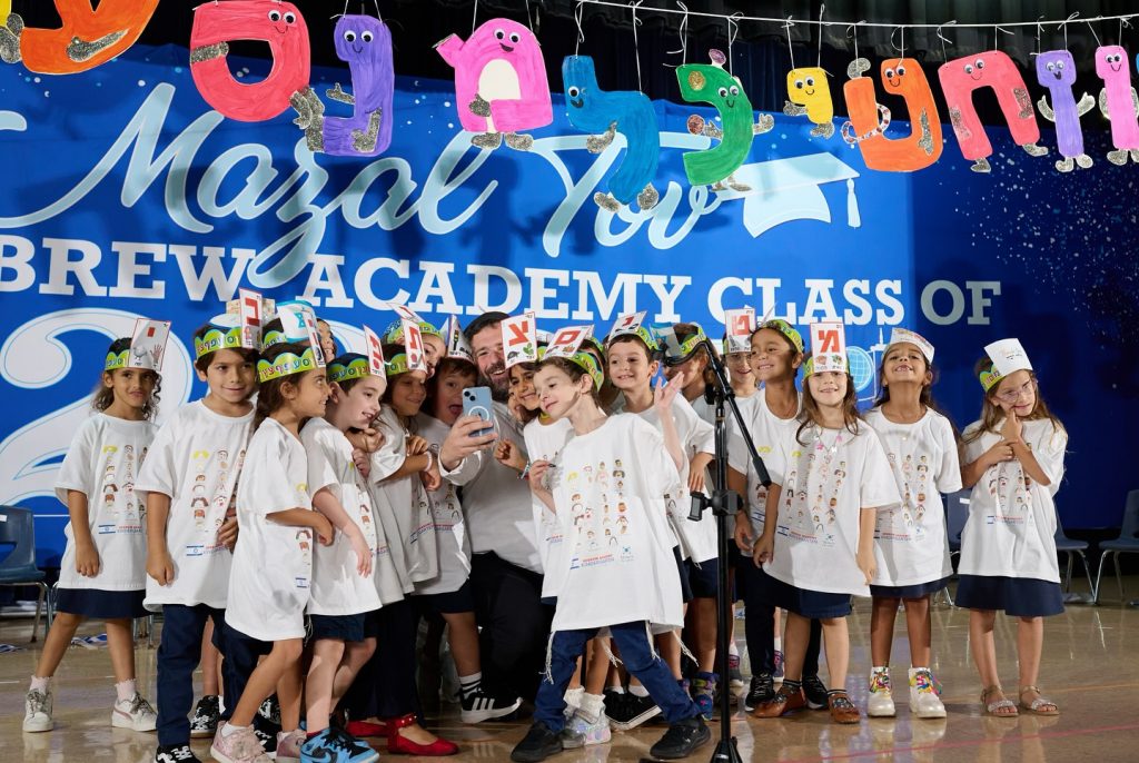 Group of children and their teacher taking a selfie on stage at an event.