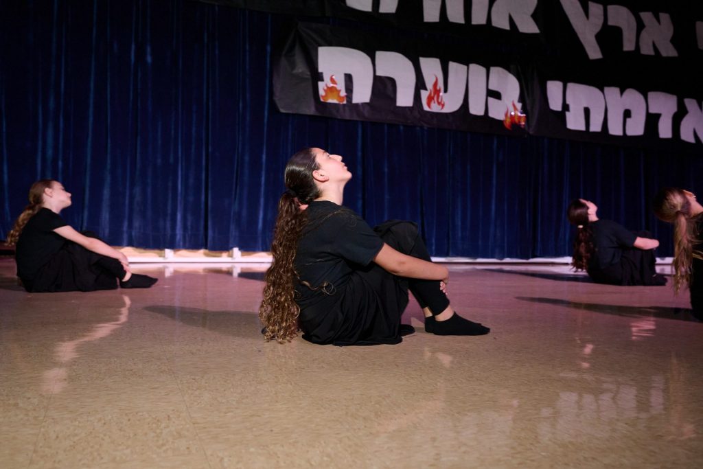 Four girls sitting on a dance floor with their heads looking up.