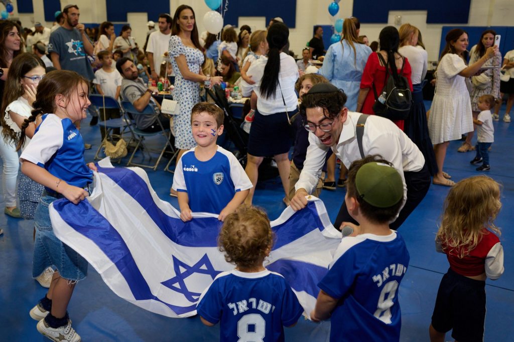 One male and several small children holding an Israeli flag, celebrating at a large event.