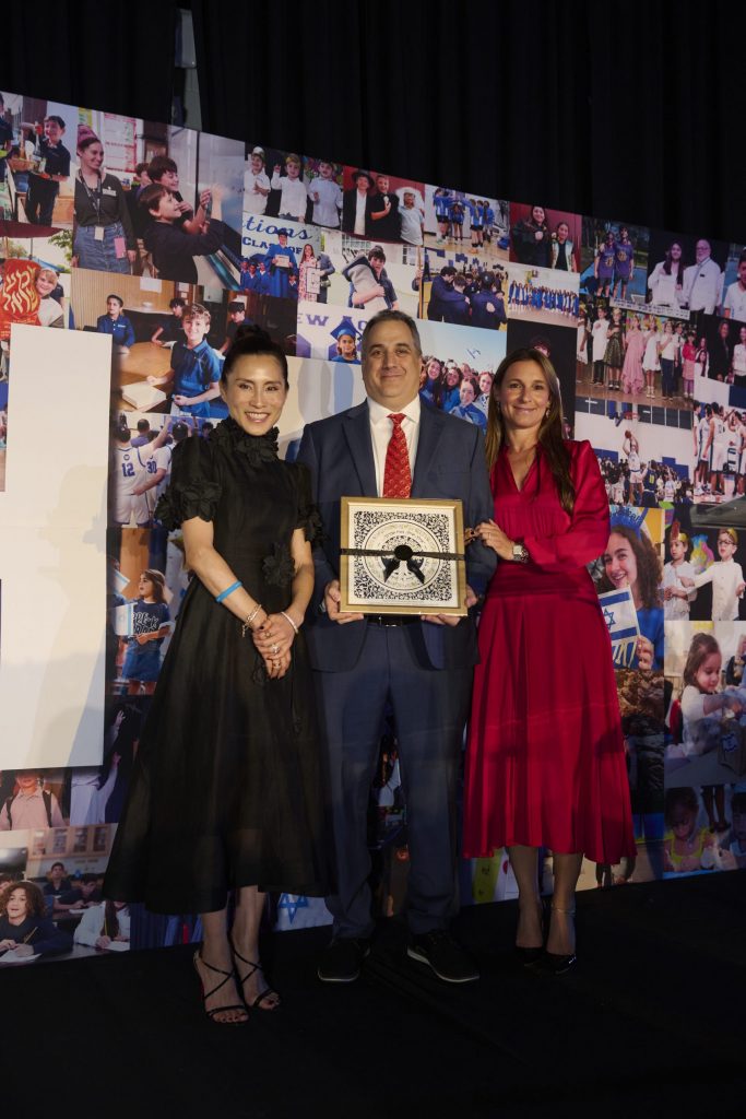 Two women and a man holding a gift-wrapped picture at Hebrew Academy's 76th Annual Light event.