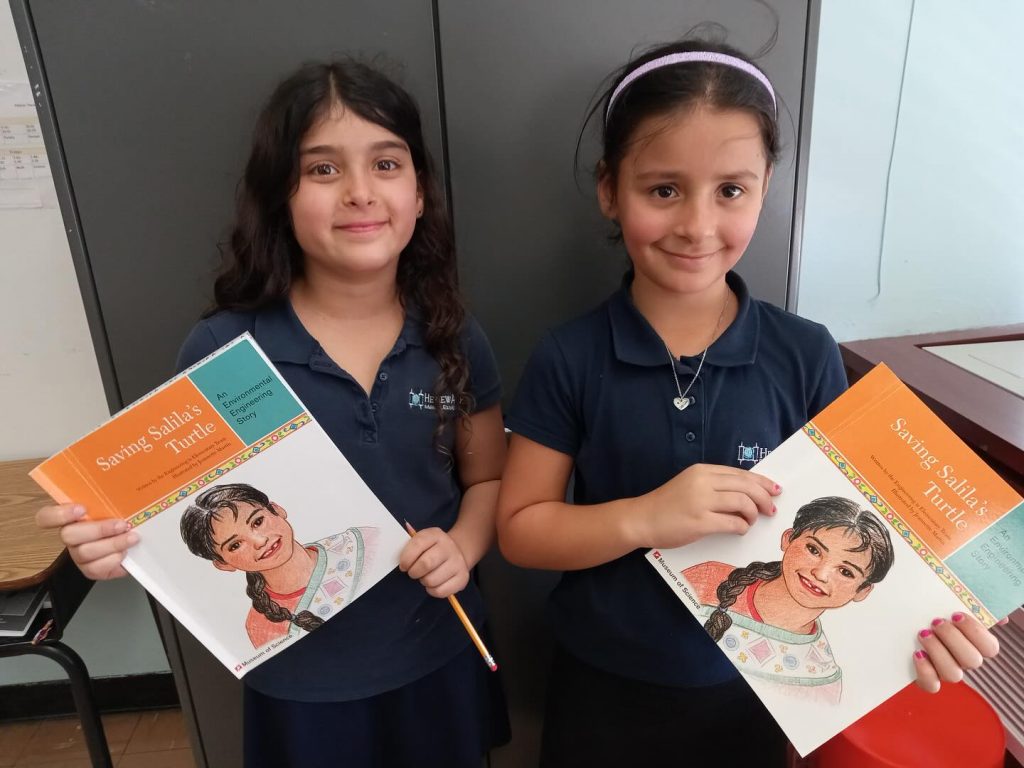 Two kids happily holding a book and smiling.