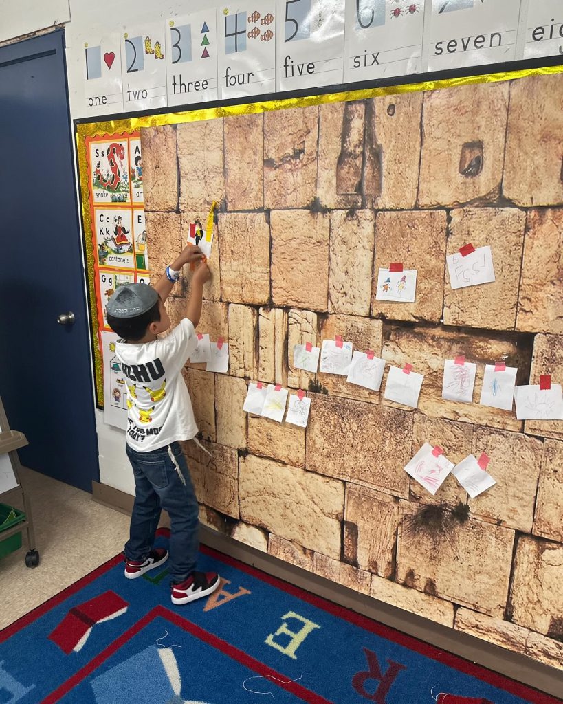 Small child placing stickers on a wall covered with various stickers in a classroom.